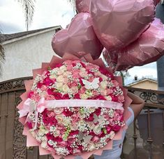 a bouquet of pink and white flowers in front of a gate with balloons attached to it