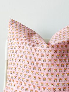 a pink pillow with orange and white flowers on the front, sitting against a white wall