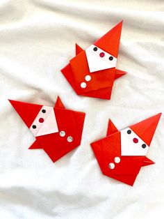 three red origami foxes are on a white sheet and one is wearing a santa hat