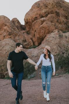 a man and woman holding hands while walking through the desert with large rocks in the background