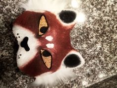 a red and white animal mask with black spots on it's face sitting on a granite surface