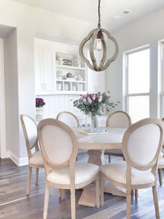 a chandelier hangs over a dining room table with beige chairs and white walls