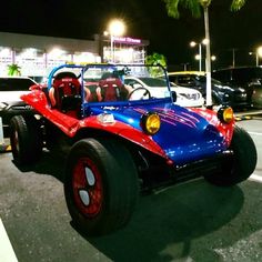 a red and blue car parked in a parking lot at night with other cars behind it