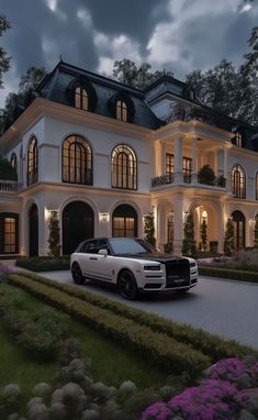 a white car is parked in front of a large house at night with lights on