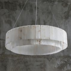 a white circular light fixture hanging from a metal rod in a concrete room with grey walls