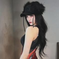 a woman with long black hair wearing a furry hat and red dress is standing in front of a wall