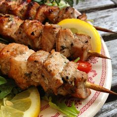 a plate topped with meat and veggies on skewers next to lemon wedges