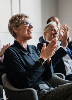 an older woman clapping while sitting in a chair with two other people behind her,