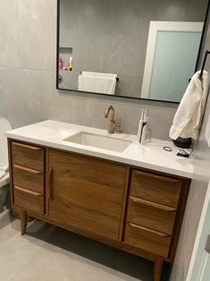 a white toilet sitting next to a bathroom sink under a mirror on top of a wooden cabinet