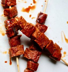 several skewers of meat sitting on top of a white plate covered in sauce