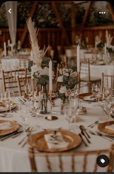 the table is set with white linens, gold chargers and tall centerpieces