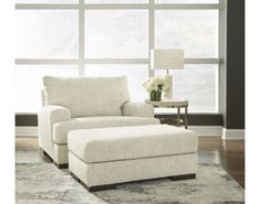 a white chair and ottoman in front of a large window with flowers on the table