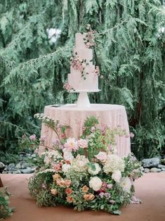 a wedding cake sitting on top of a table covered in flowers and greenery next to trees