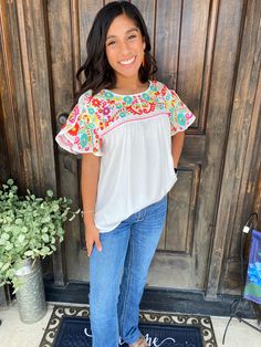 a woman standing in front of a door wearing jeans and a top with flowers on it