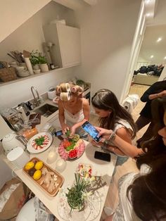 three women standing around a table with food on it and one woman taking a photo