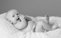 a black and white photo of a baby laying on a blanket with his hands in his mouth