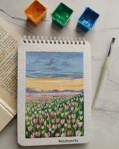 an open book next to some watercolor paints and a drawing of tulips