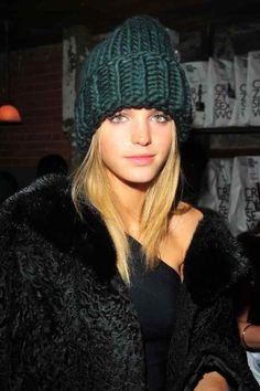 a woman with blonde hair wearing a green knitted hat and fur coat, looking at the camera