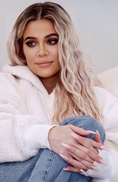 a woman sitting on top of a couch with her hands folded over her chest and looking at the camera