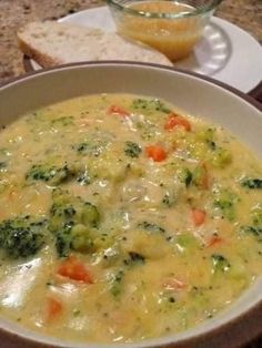 a bowl of soup with broccoli, carrots and bread on the side