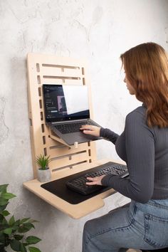 a woman sitting at a desk using a laptop computer on a wooden shelf that holds a keyboard and mouse