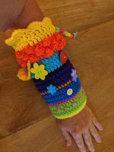 a child's hand wearing colorful crocheted arm warmers on top of a wooden floor