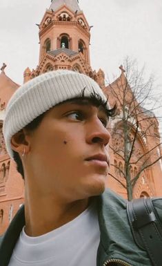 a man wearing a beanie standing in front of a building with a clock tower