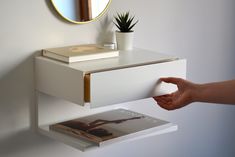 a person holding a mouse in front of a white shelf with a magazine on it