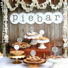 a table topped with pies and cakes next to a wooden wall covered in paper flowers