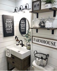 a white bathroom with black and white signs on the wall above the sink, along with two hanging shelves filled with toiletries