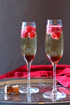 two champagne flutes with raspberries in them on a tray