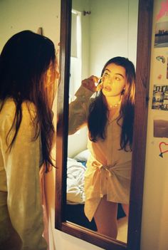 a woman brushing her teeth in front of a mirror while looking at herself in the mirror