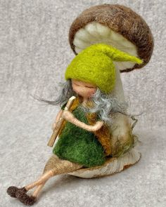 a small doll sitting on top of a mushroom with a green dress and white hair