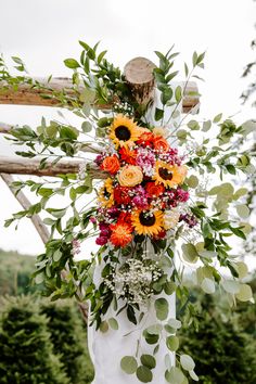 a bouquet of sunflowers and other flowers is hanging from a wooden structure