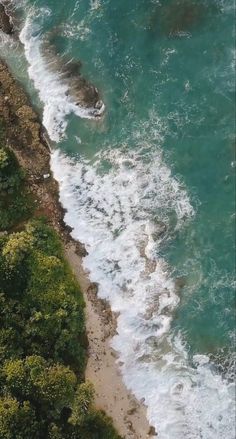 an aerial view of the ocean with waves crashing on the shore and trees in the foreground