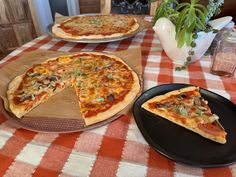 two pizzas sitting on top of a table with one slice missing from the pie