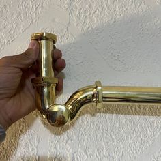 a person is holding the handle on a gold colored shower faucet in front of a white wall