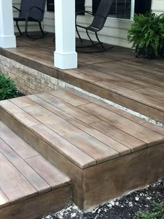 a wooden porch with steps leading up to the front door and patio furniture on either side