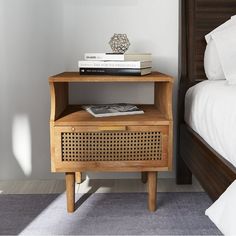 a nightstand with books on top of it next to a bed