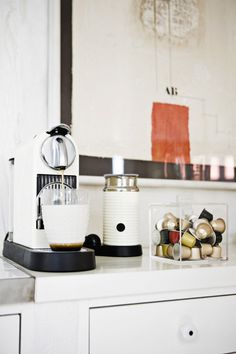 an espresso machine sitting on top of a white counter next to a blender