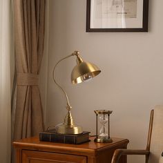 a desk lamp sitting on top of a wooden table next to a chair and window