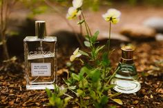 two perfume bottles sitting on the ground next to some flowers