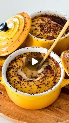 two yellow bowls filled with food on top of a wooden cutting board next to bread