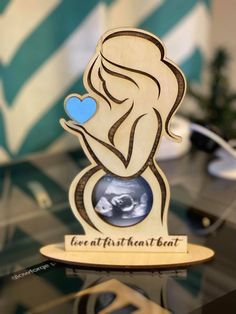 a wooden cutout of a pregnant woman holding a blue heart on top of a table