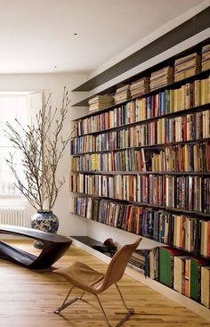 a living room filled with lots of books and furniture next to a tall book shelf