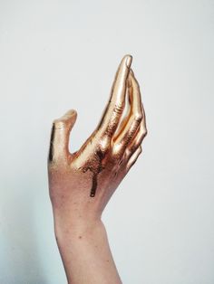 a person's hand with gold paint on it holding something up in the air