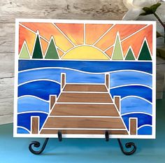 a card with a painting of a dock in the water and mountains behind it, on a blue background