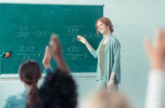 a woman standing in front of a blackboard giving a lecture to her class mates