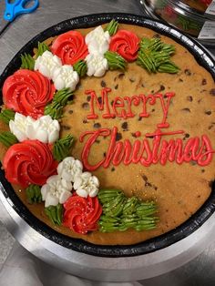 a merry christmas cake decorated with red and white flowers on a silver platter next to scissors