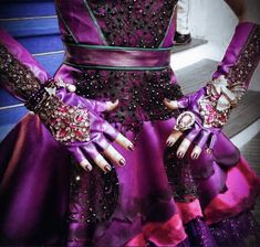 a close up of a person wearing purple dress and gloves with jewels on their hands